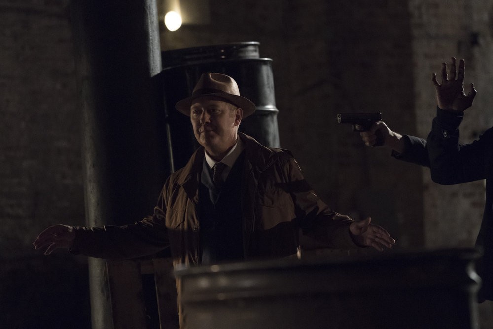 Raymond Reddington (James Spader) menacé d'une arme lève les bras
