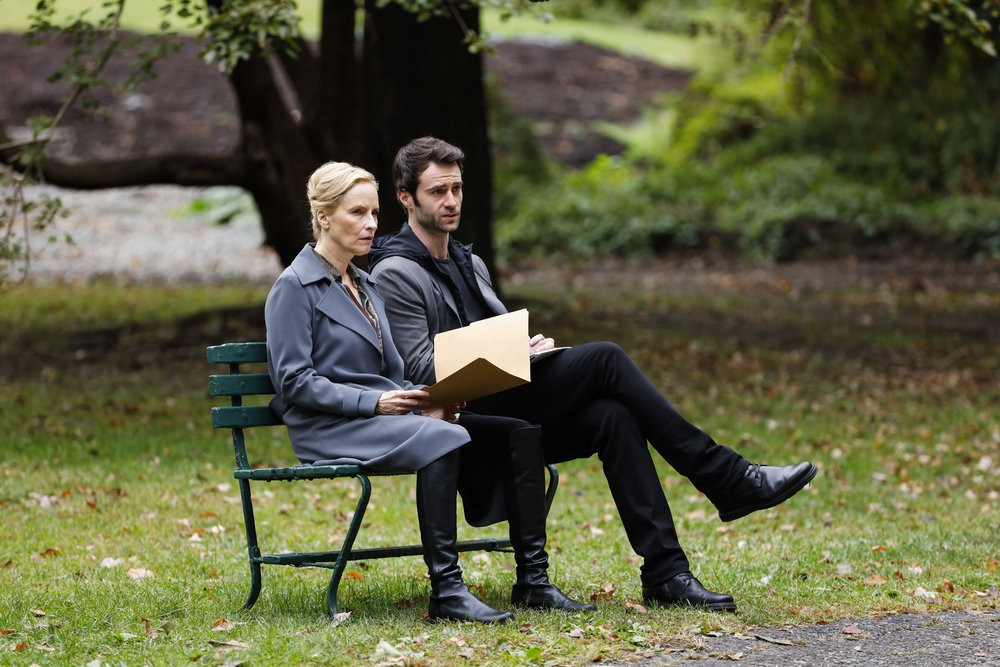  Katarina Rostova (Laila Robins) assise côte à côte avec Skip Sutherland (Cillian O'Sullivan) sur un banc dans un parc