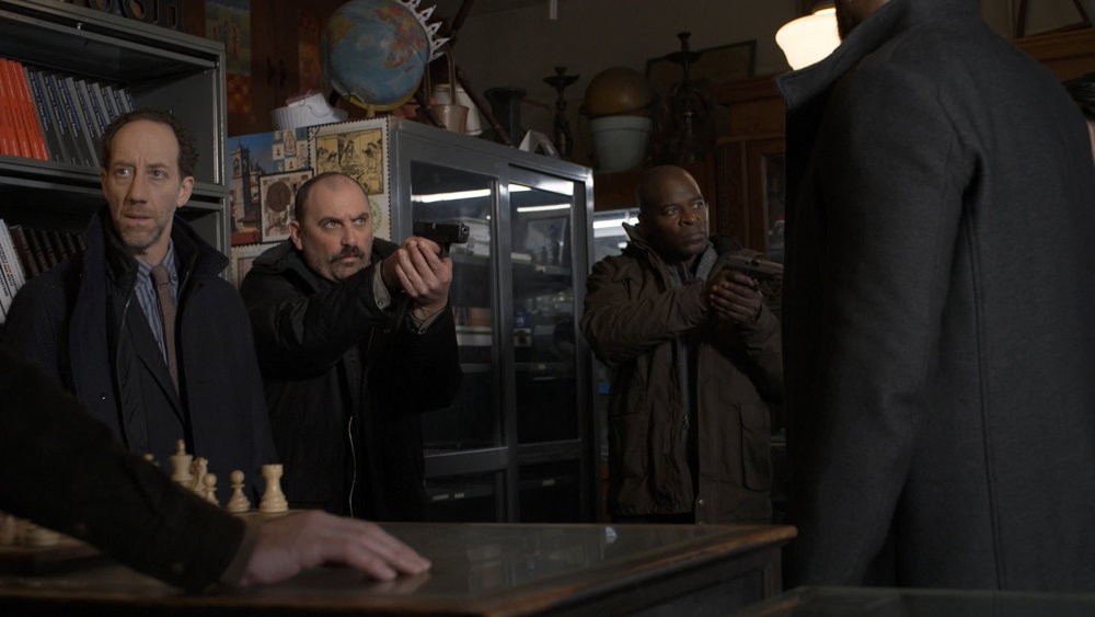 Frank Merwin (Joey Slotnick) avec deux acolytes de Reddington à ses côtés armes au poing,  Morgan (Genson Blimline) et Dembe (Hisham Tawfiq) 