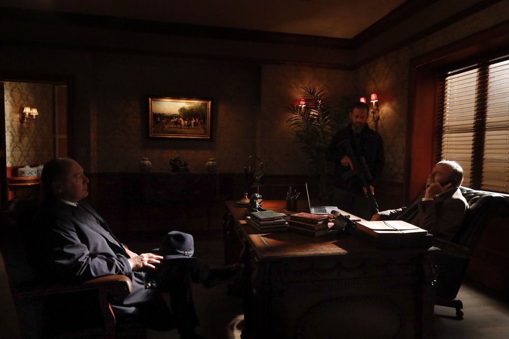 Raymond Reddington (James Spader) et son homme de main Chuck (Jonathan Holtzman) qui a une arme à la main menacent Heidegger (Michael Pemberton) pour qu'il téléphone