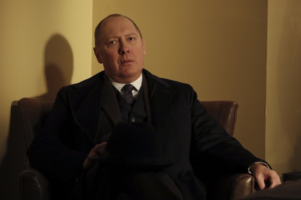 Raymond Reddington (James Spader) assis dans un fauteuil, fedora sur son genoux, semble inquiet