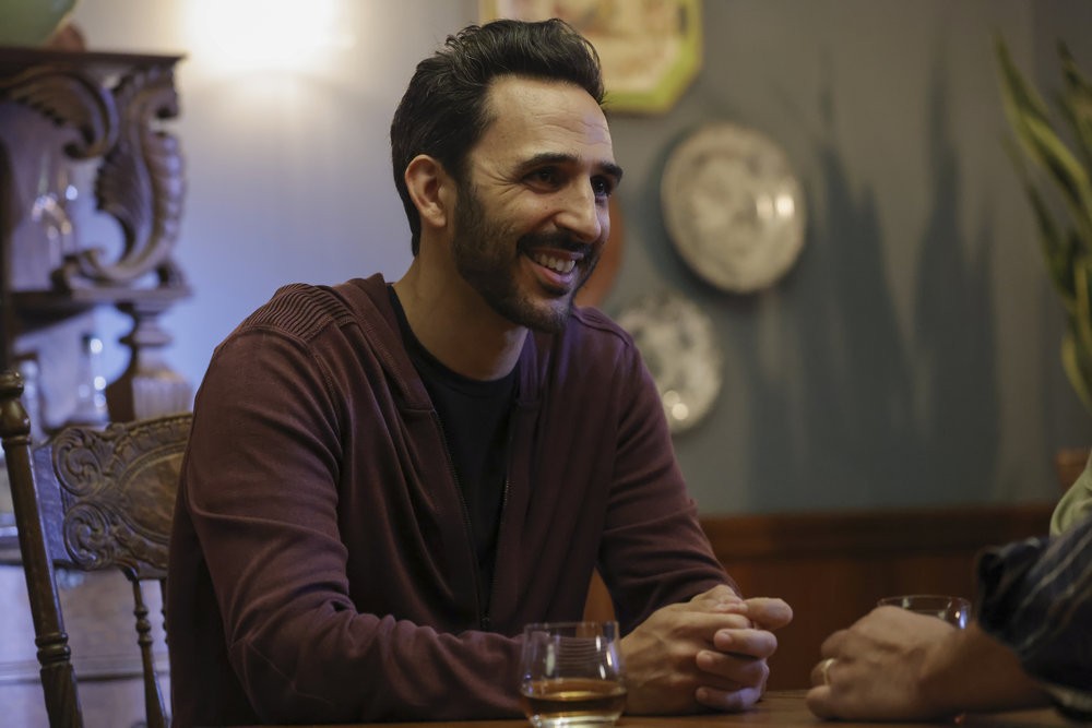 Aram (Amir Arison) souriant devant une verre chez son ancien patron Harold Cooper