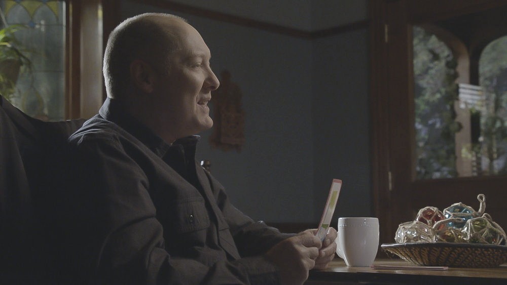 Raymond Reddington (James Spader) assis chez les Cooper, une carte en main