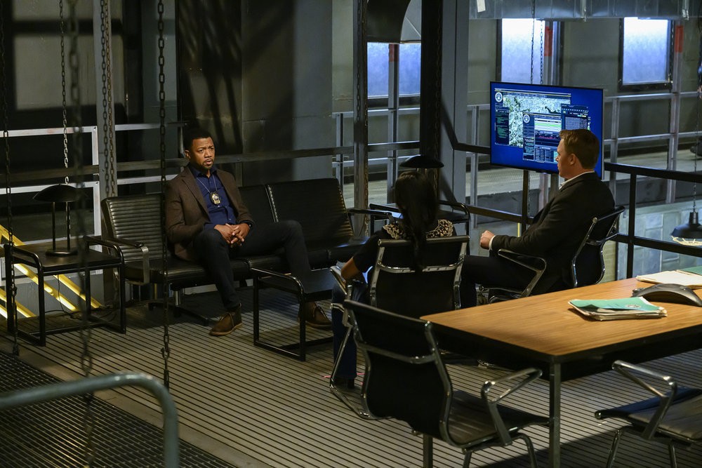 Le détective Patrick Fleming (Miles Mussenden) parlent avec les agents Ressler et Malik dans la salle commune du Bureau de Poste