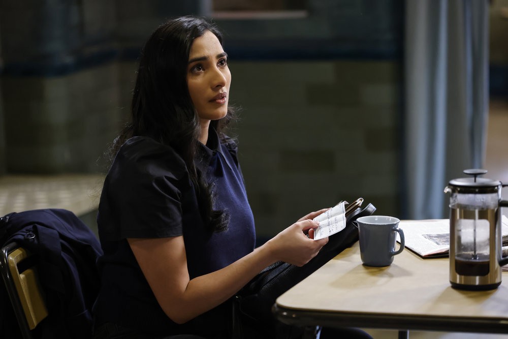 Siya Malik  (Anya Banerjee), assise dans la planque de Reddington, tient à la main ce qui ressemble à un chèque au porteur