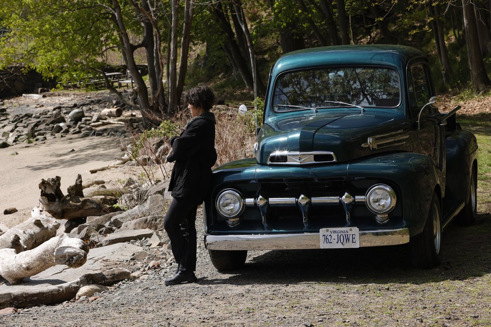 Weecha ( Diany Rodriguez) attend les bras croisés près d'une vieille Ford