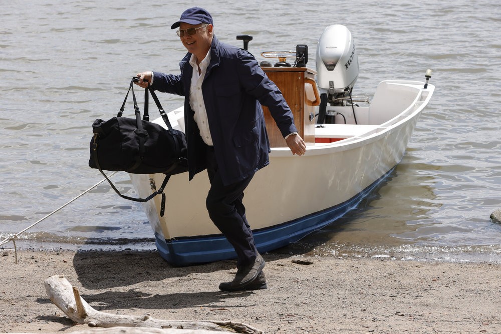 Raymond Reddington (James Spader) très souriant et  un sac à la main vient de mettre pied à terre sur une petite plage